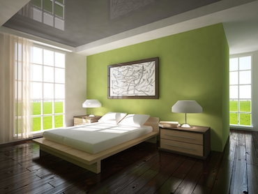 room with a hardwood floor, bright windows on two sides, and a two person bed with a bedside table and lamp on each side